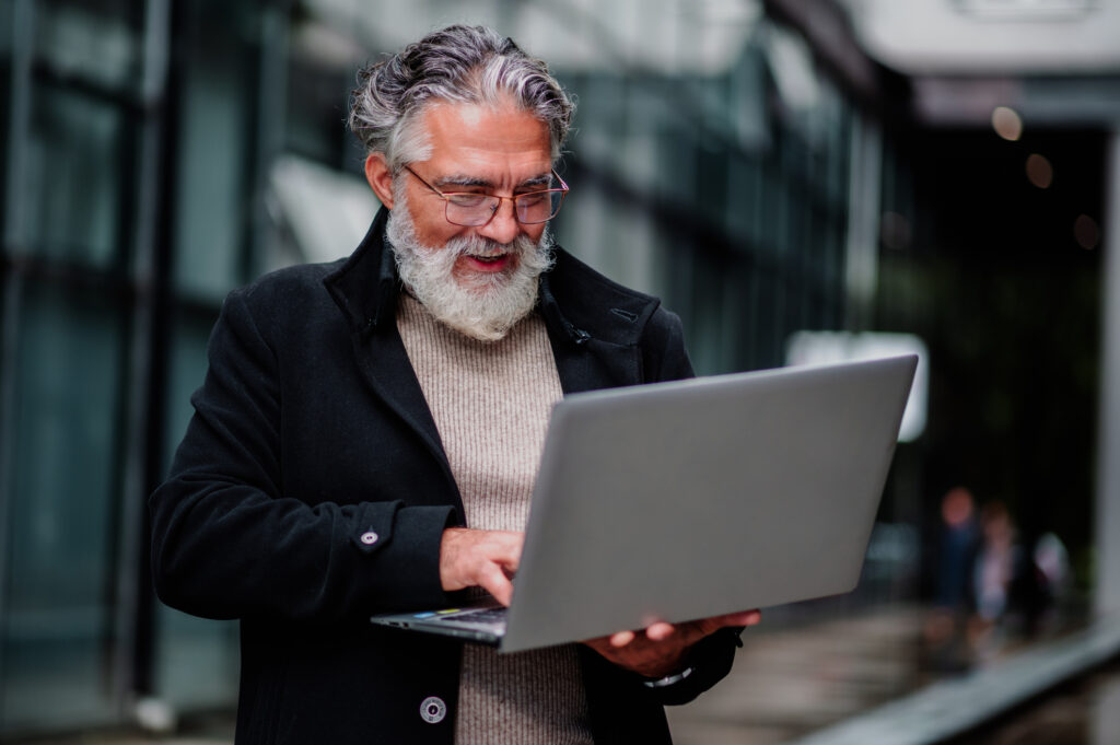 Portrait of a senior businessman using laptop and sitting on a bench outside